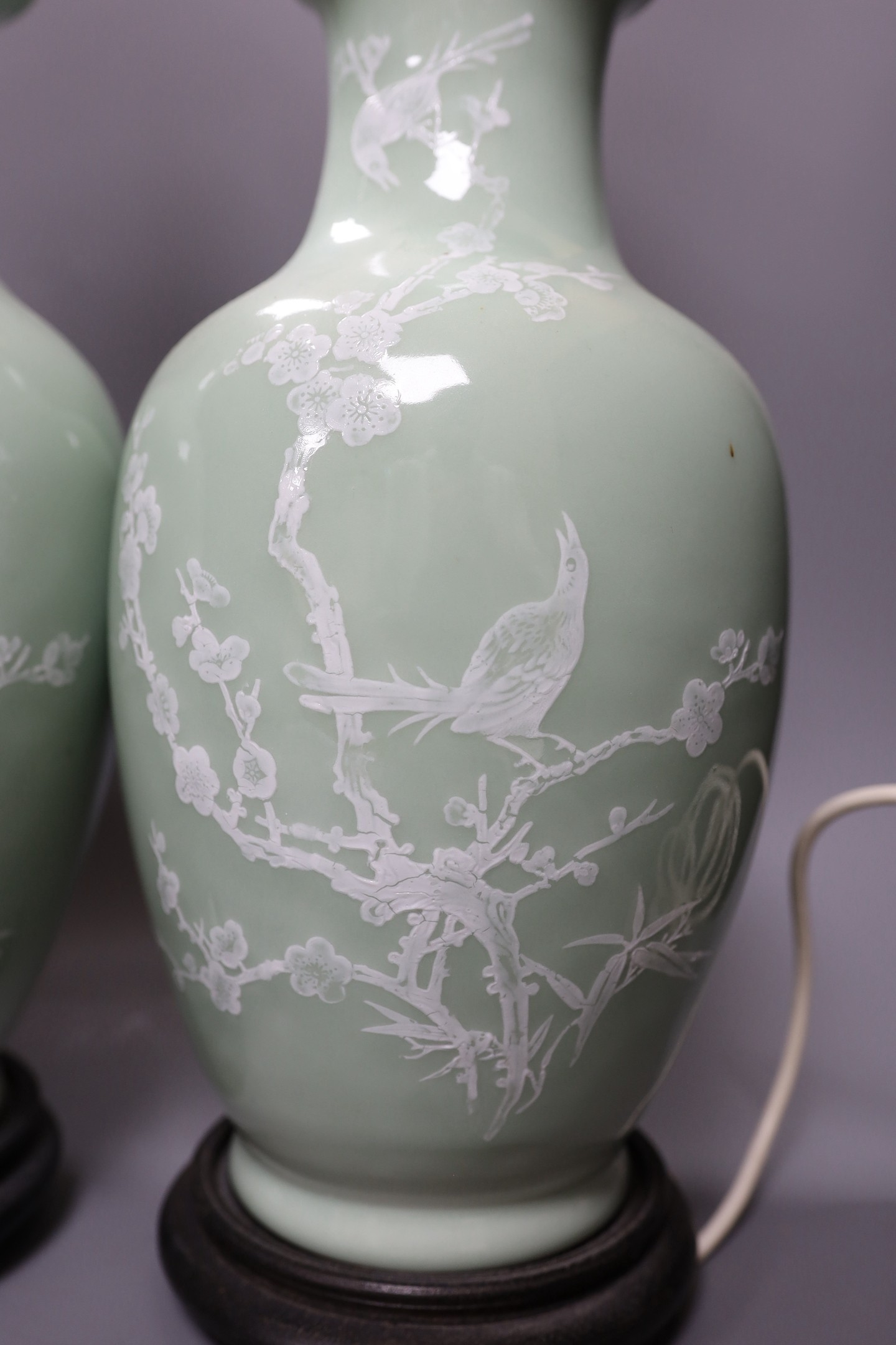 A pair of Chinese slip decorated celadon ground lamps, 40cms high including stands